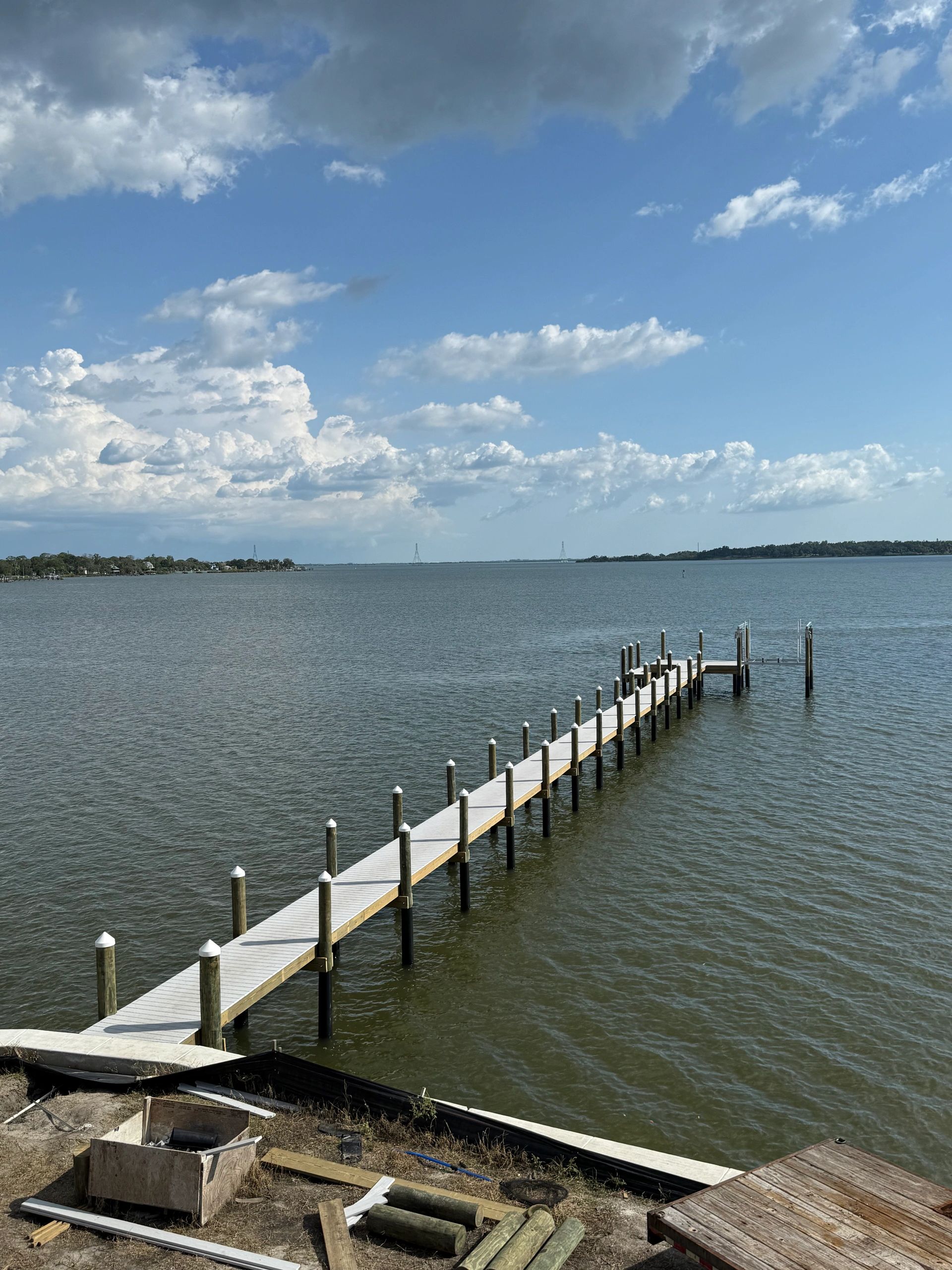 A long wooden dock extending into a calm body of water under a partly cloudy sky.