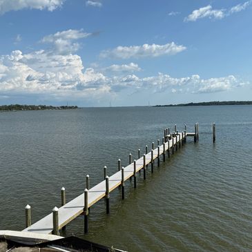 A long wooden dock extending into calm water under a partly cloudy sky.