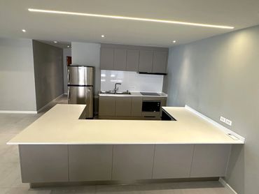 Modern kitchen with an L-shaped white countertop and gray cabinets.