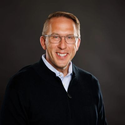 Smiling man with glasses in a black sweater against a dark background.