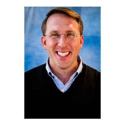 Smiling man in glasses, black sweater, and blue shirt with blue background.