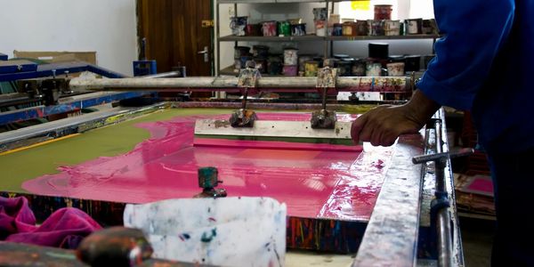 A person screen printing with bright pink ink in a workshop.