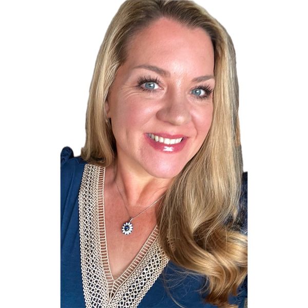 Smiling woman with long blonde hair wearing a blue top with lace detail and a floral pendant necklace.