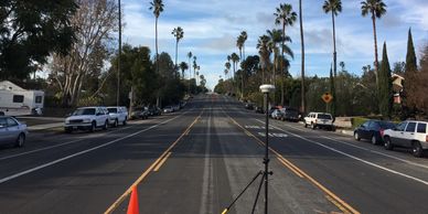 Empty street with survey equipment and cars parked on both sides.