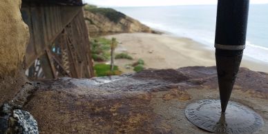 Pointed metal object on a rusty surface with a beach in the background.