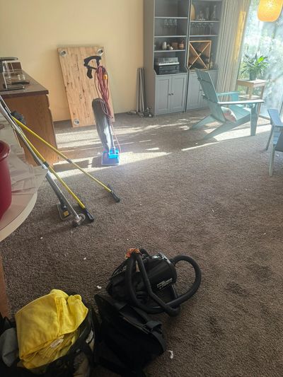 Sunlit living room during cleaning with a vacuum cleaner, mop, and professional cleaning supplies.