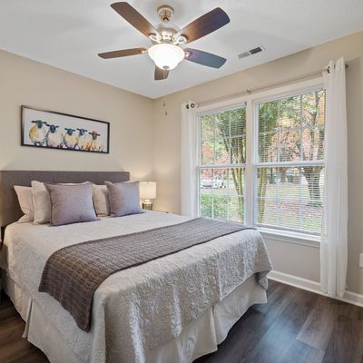 a bedroom with a king size bed with wall art above. window with open blinds and a ceiling fan. 