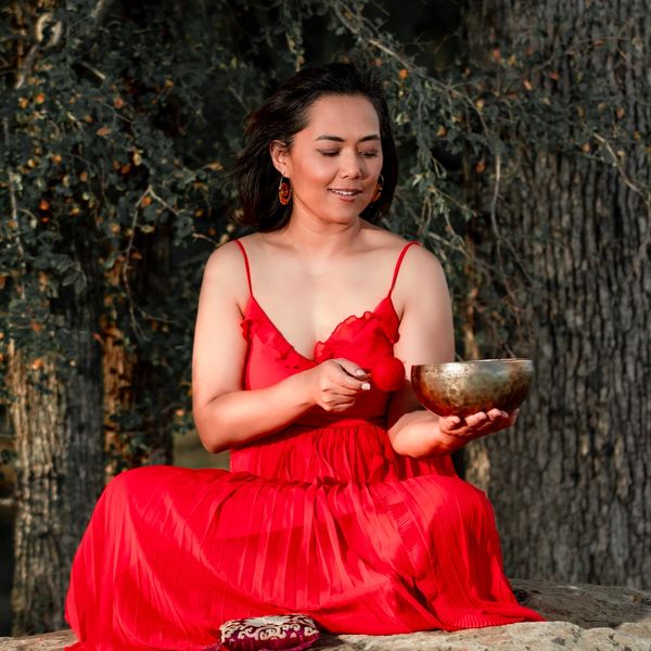Woman in red dress holding a singing bowl outdoors.