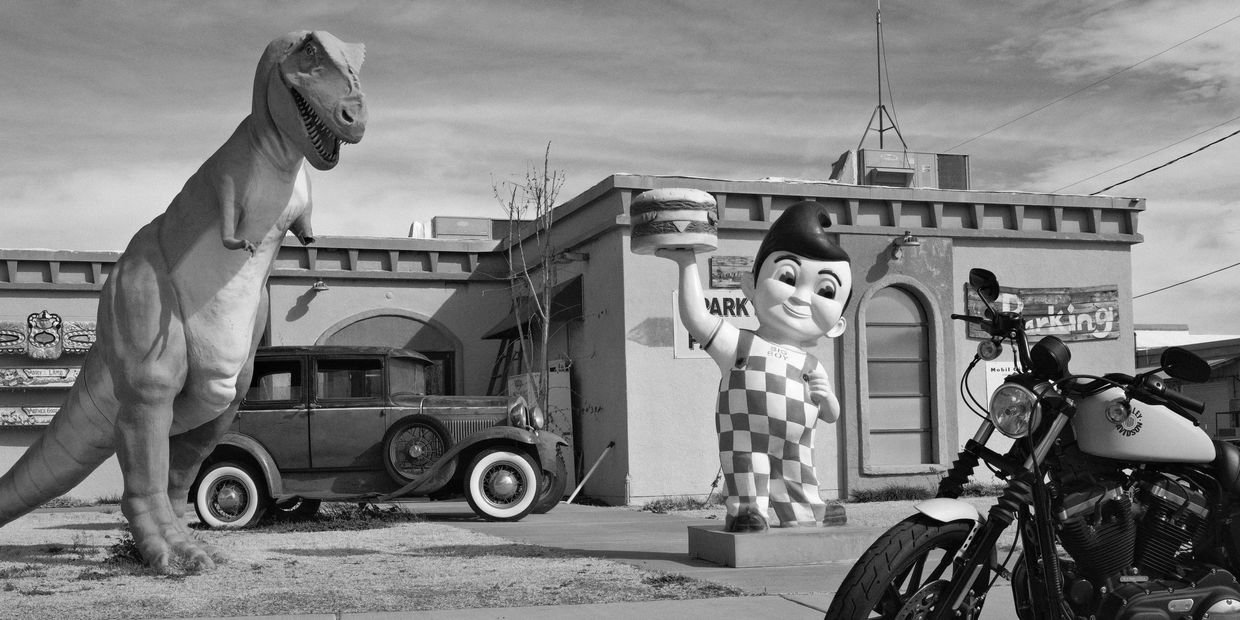 Vintage scene with a dinosaur statue, classic car, Big Boy statue, and motorcycle.