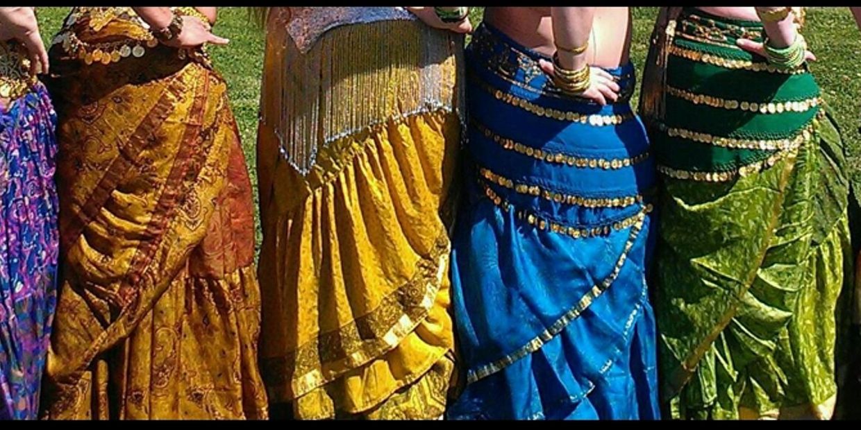 Women wearing colorful cultural skirts with gold coin decorations.