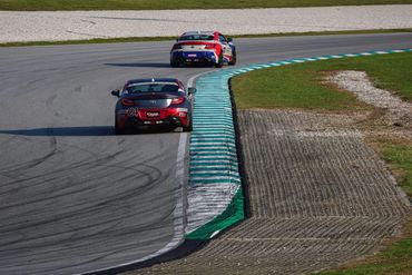 Two race cars navigate a curving track during a motorsport event.