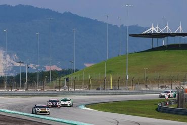 Race cars speeding on a curved racetrack with mountains in the background.