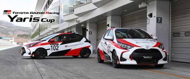 Two Toyota Gazoo Racing Yaris Cup cars parked in front of pit garages.