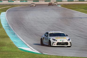 White race car leading on a curved racetrack with others behind.