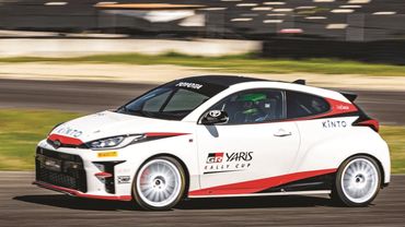 White Toyota GR Yaris rally car speeding on a racetrack.