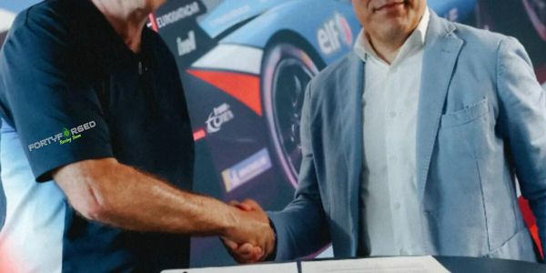 Two men shaking hands over a table with Alpine Endurance Team and Devoteam logos.