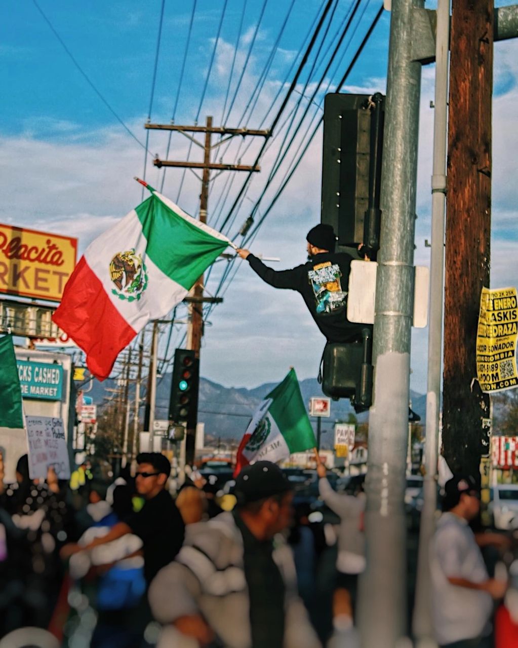 Person waving Mexican flag during a street protest with crowd and signs.