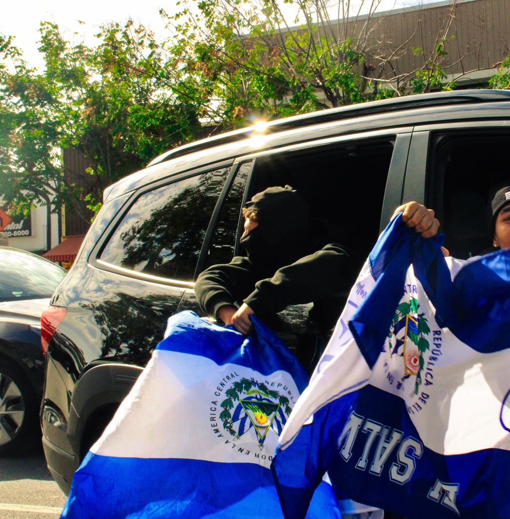 Two people holding and waving Nicaraguan flags outside a vehicle.