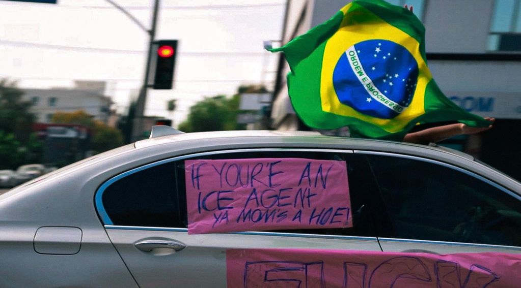 Person holding Brazilian flag out of car window with a sign on the car.