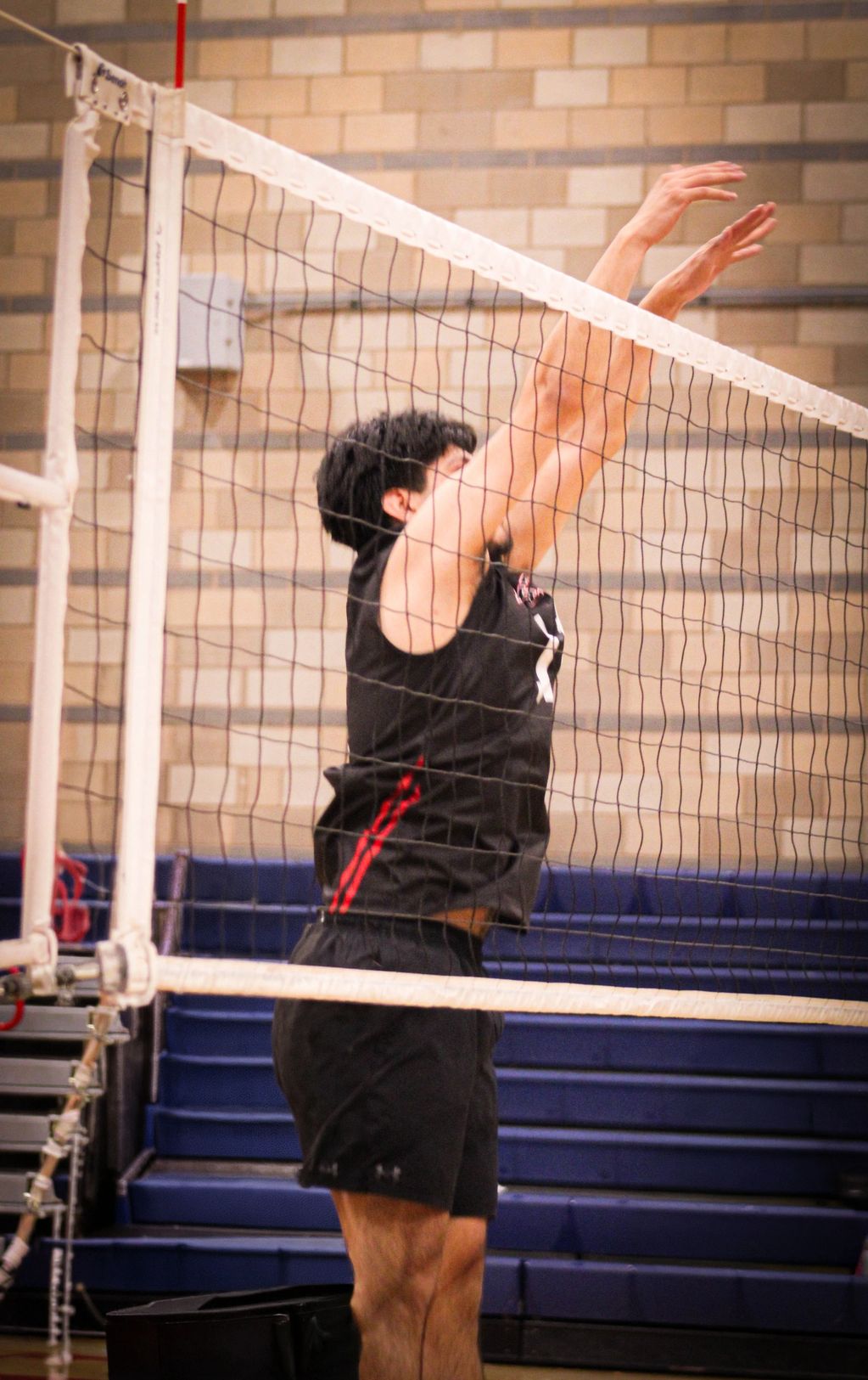 Volleyball player jumping to block at the net in a gym.