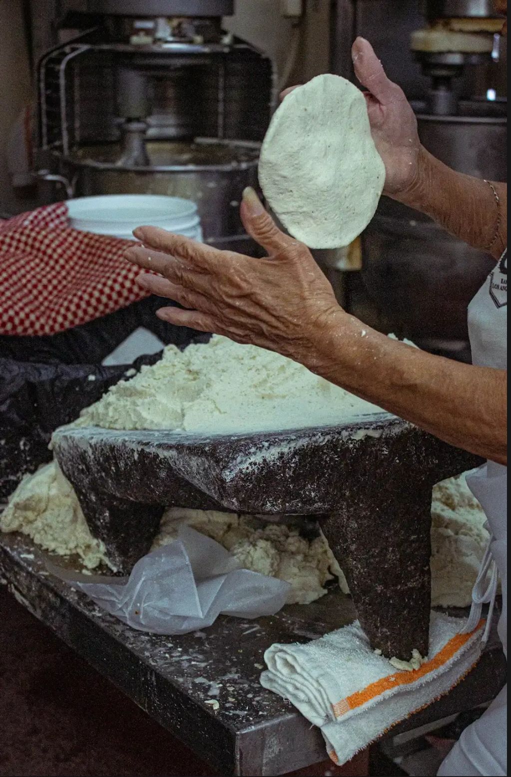Hands shaping dough on a traditional stone grinder with flour scattered around.