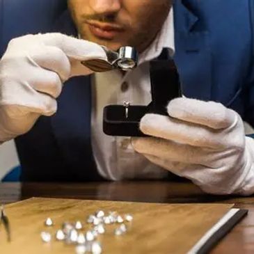 A jeweler inspecting diamonds with a loupe while wearing white gloves.