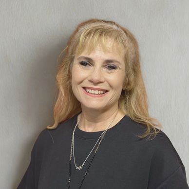 Smiling woman with blonde hair wearing a black top and necklace.