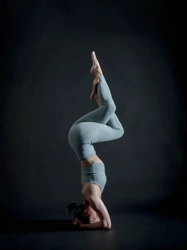 Woman performing a complex yoga headstand pose in gray activewear.