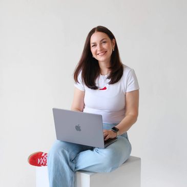 Young woman sitting with a laptop, smiling at the camera.