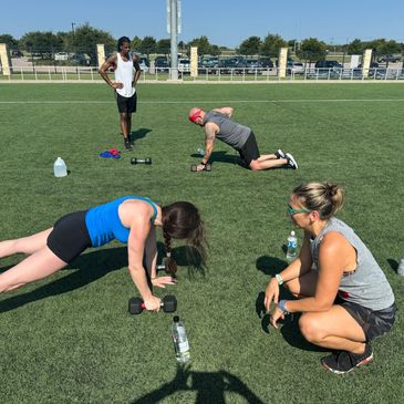 Group workout on grass with dumbbells and water bottles.