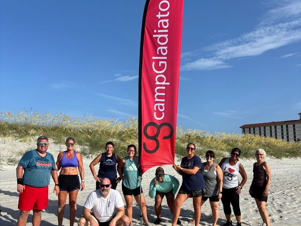 Group photo at a beach with a campGladiator flag.
