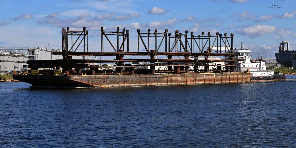A barge carrying large metal structures on a river or harbor.