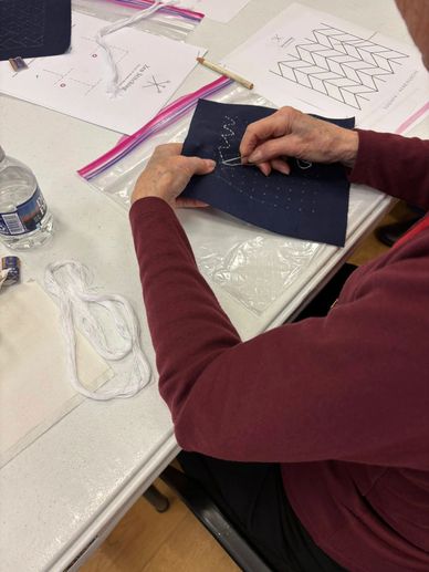 Person hand-stitching a pattern onto dark fabric with embroidery thread.