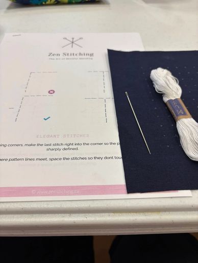 Embroidery kit with needle, white thread, and instructions on a table.