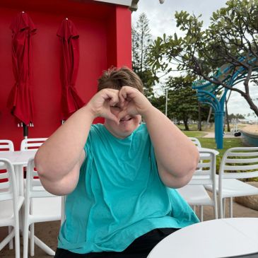 Person making a heart shape with hands at an outdoor cafe.