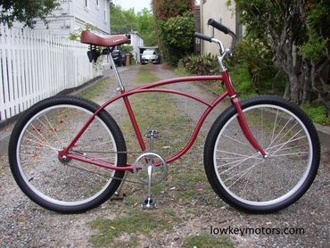 Classic red cruiser bicycle parked on a gravel driveway beside a white picket fence.