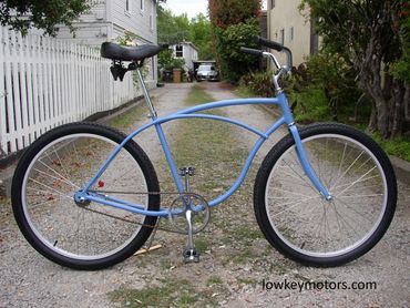 Light blue cruiser bike parked on a gravel path beside a white fence.