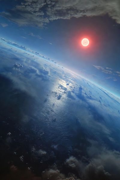 A glowing red sun rises above Earth's horizon with clouds and ocean below.