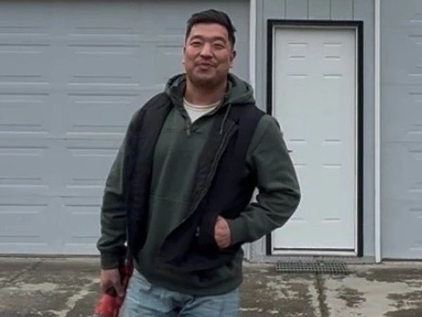 Man in casual clothes standing outside garage with a red object in hand.