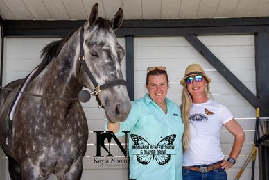 Two women smiling with a gray horse at an equestrian event.
