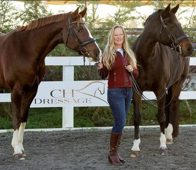 A woman stands between two horses at a dressage training facility.