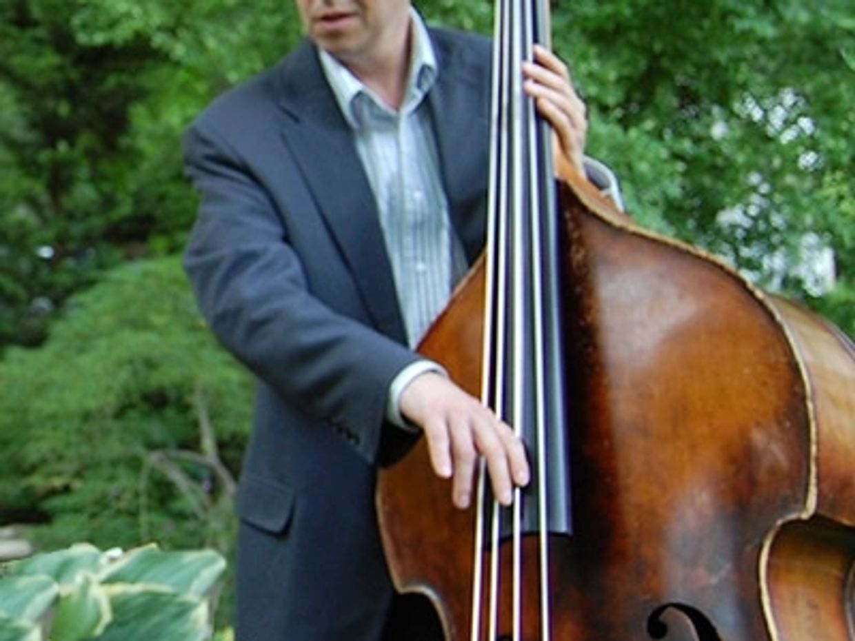 Man in a suit playing a double bass outdoors.