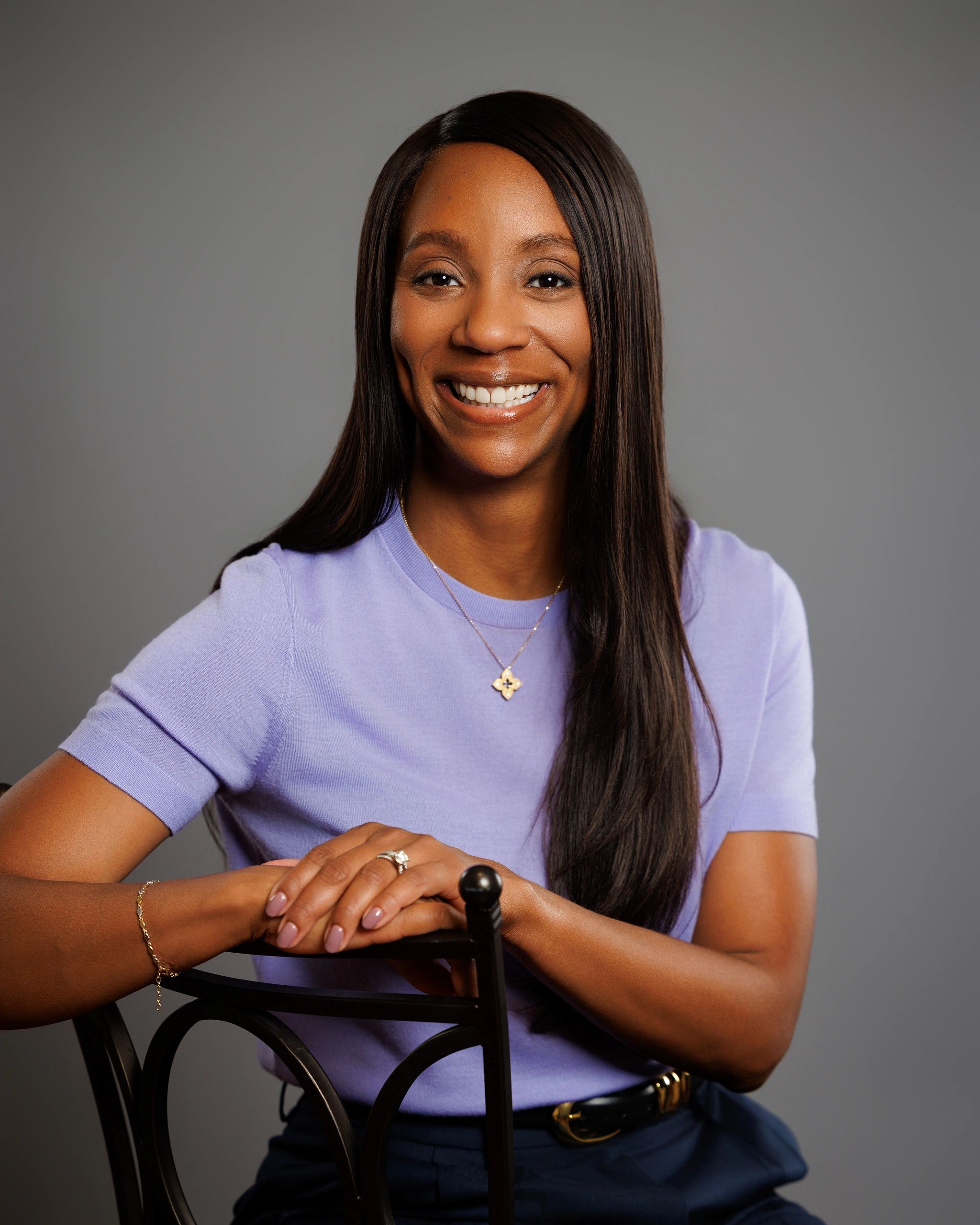Smiling woman in a purple top sitting on a chair.