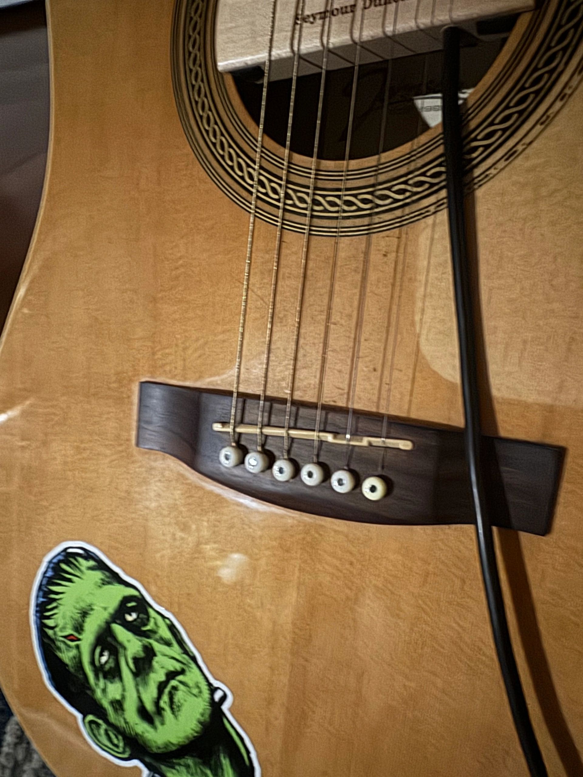 Close-up of an acoustic guitar with a green Frankenstein sticker.