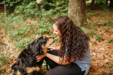 Woman lovingly interacts with her dog in a wooded area.