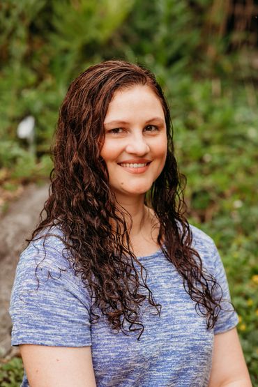 Smiling woman with curly hair in a blue shirt outdoors.