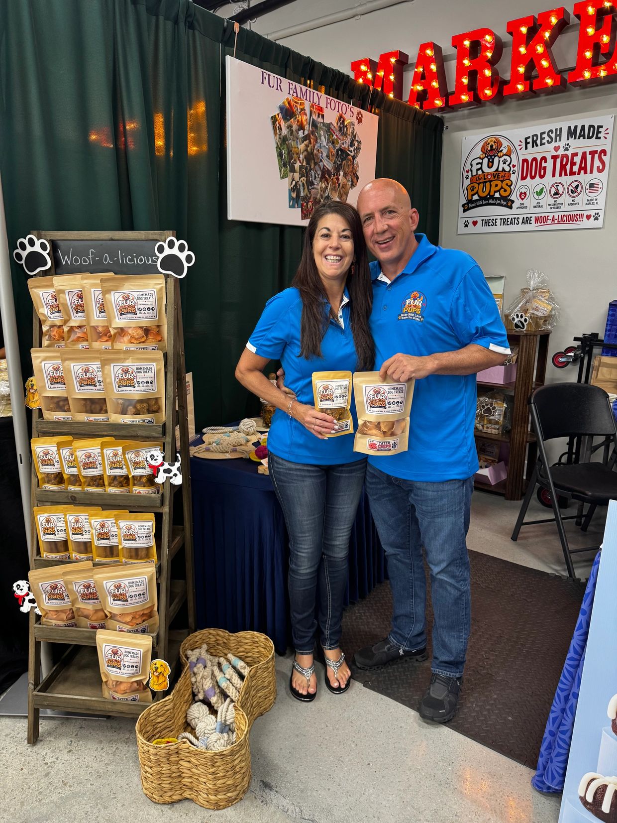 Smiling couple holding dog treats at a pet market booth.