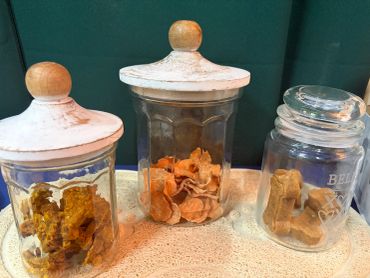 Three glass jars with wooden lids containing dried herbs or roots.