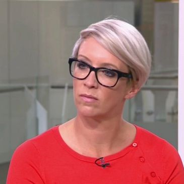 Woman with short blonde hair and black glasses wearing a red top.