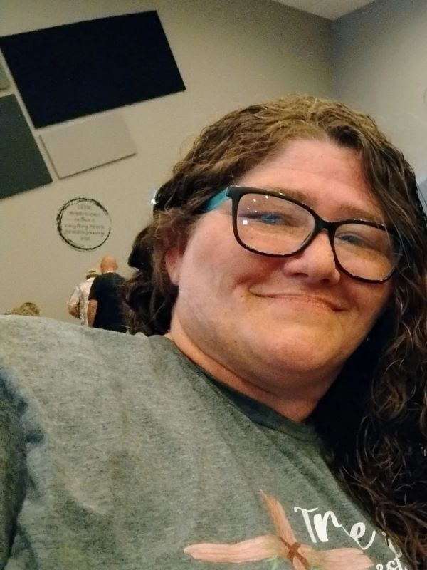 Smiling woman with glasses and curly hair taking a selfie indoors.